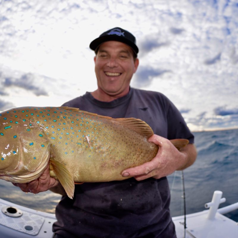a man posing for the camera holding up the fish he caught with airlie beach fishing charters in airlie beach, queensland