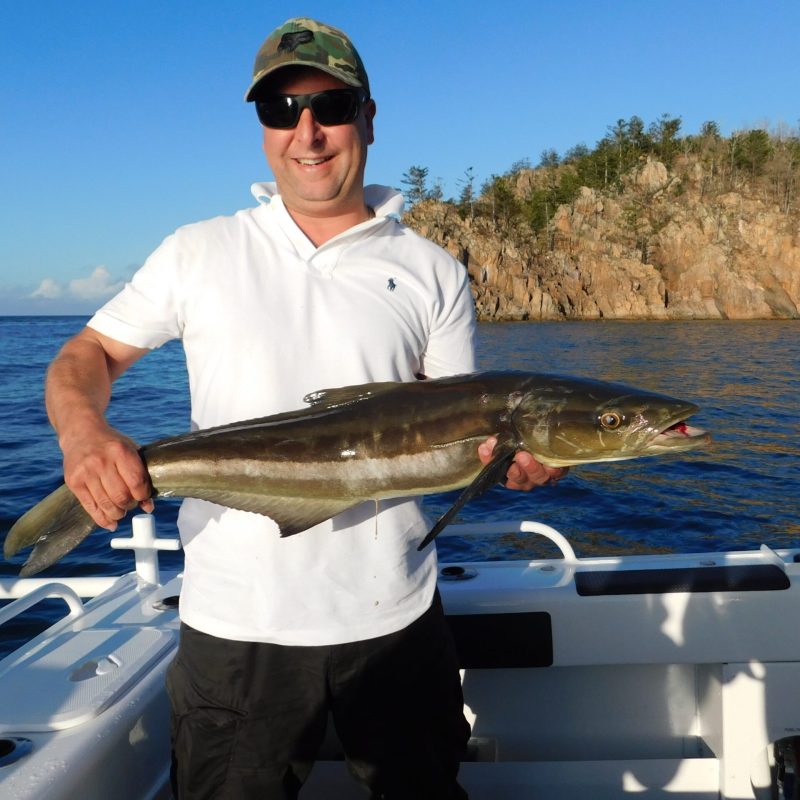 a man posing for the camera holding up the fish he caught with airlie beach fishing charters in airlie beach, queensland