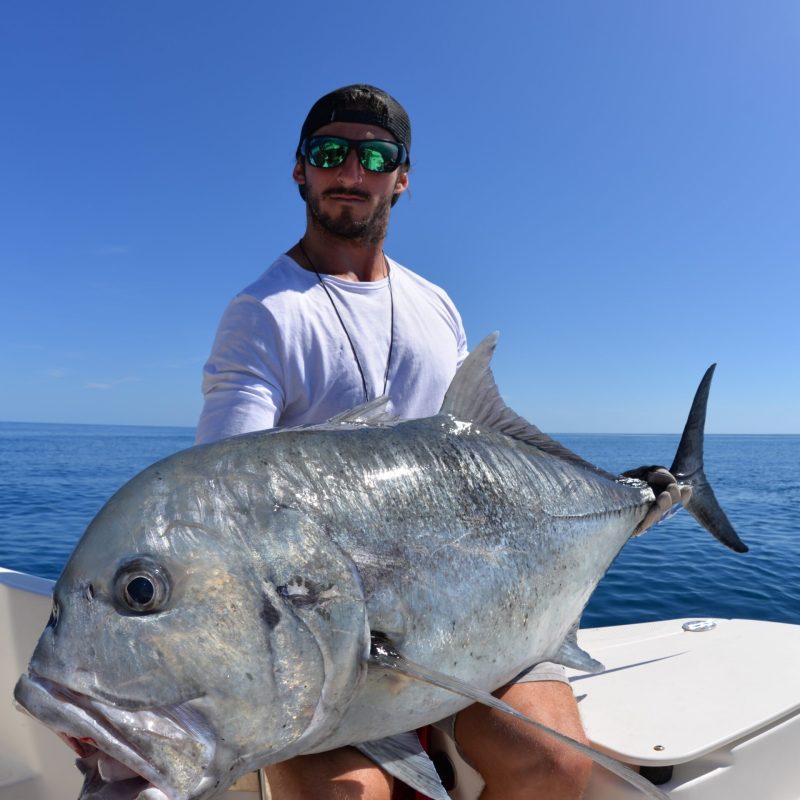 a man posing for the camera holding up the fish he caught with airlie beach fishing charters in airlie beach, queensland