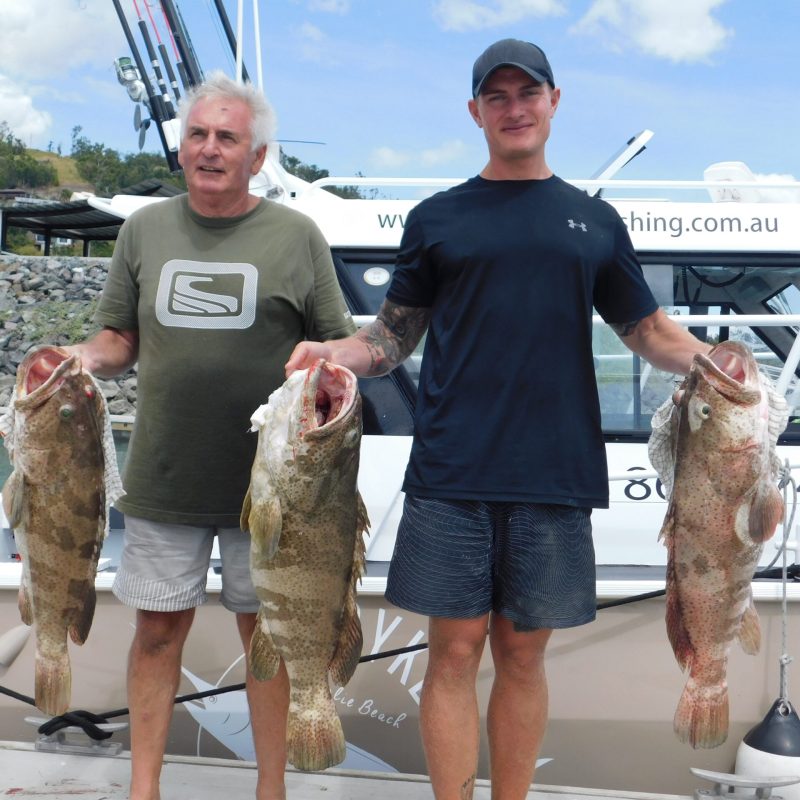 father and son posing for the camera holding up the fish they caught with airlie beach fishing charters in airlie beach, queensland