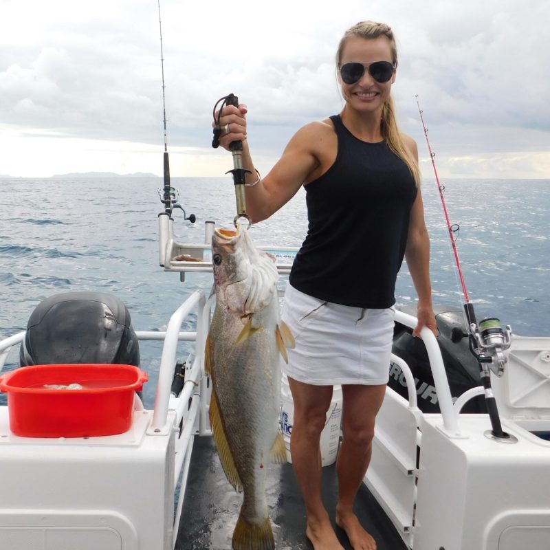 a woman posing for the camera holding up the fish she caught with airlie beach fishing charters in airlie beach, queensland