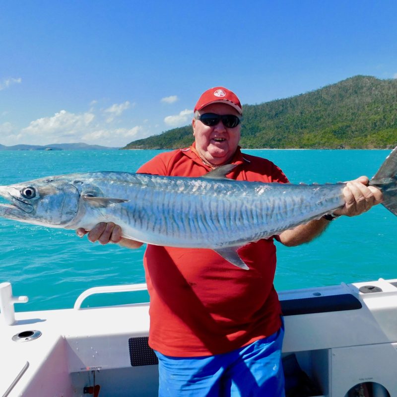 a man posing for the camera holding up the fish he caught with airlie beach fishing charters in airlie beach, queensland