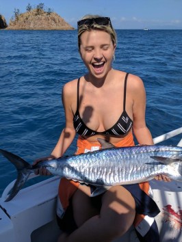 a woman posing for the camera holding up the fish she caught with airlie beach fishing charters in airlie beach, queensland