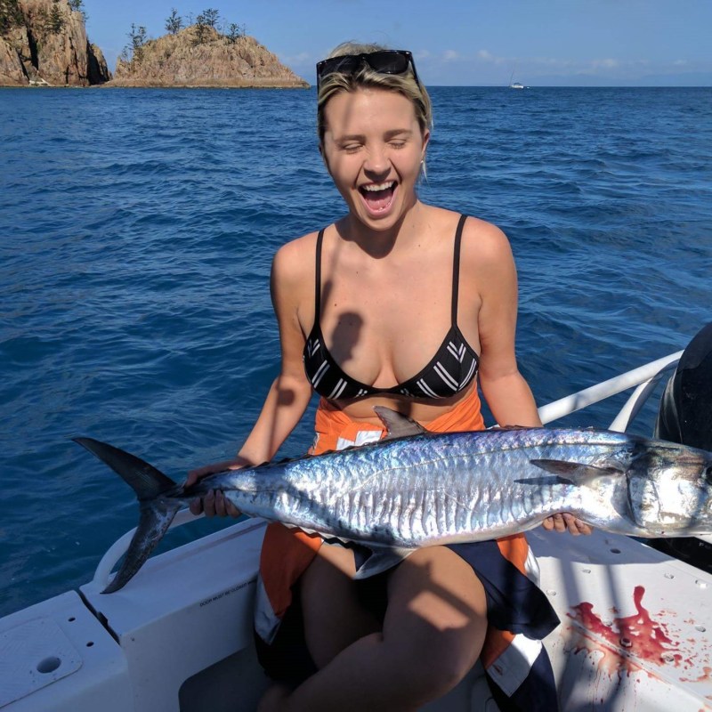 a woman posing for the camera holding up the fish she caught with airlie beach fishing charters in airlie beach, queensland
