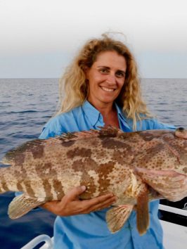 a woman posing for the camera holding up the fish she caught with airlie beach fishing charters in airlie beach, queensland