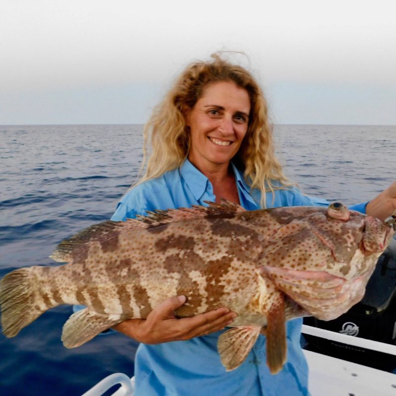 a woman posing for the camera holding up the fish she caught with airlie beach fishing charters in airlie beach, queensland