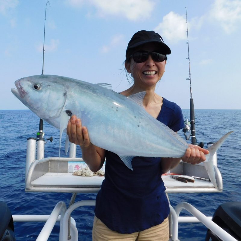 a woman posing for the camera holding up the fish she caught with airlie beach fishing charters in airlie beach, queensland
