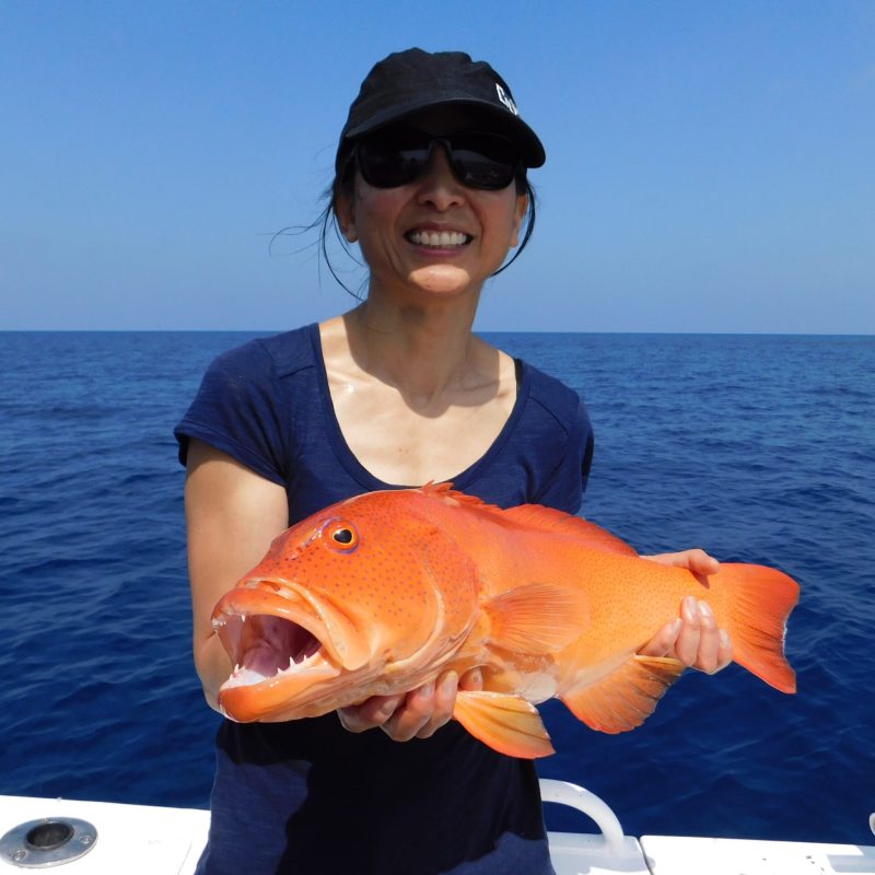 a woman posing for the camera holding up the fish she caught with airlie beach fishing charters in airlie beach, queensland