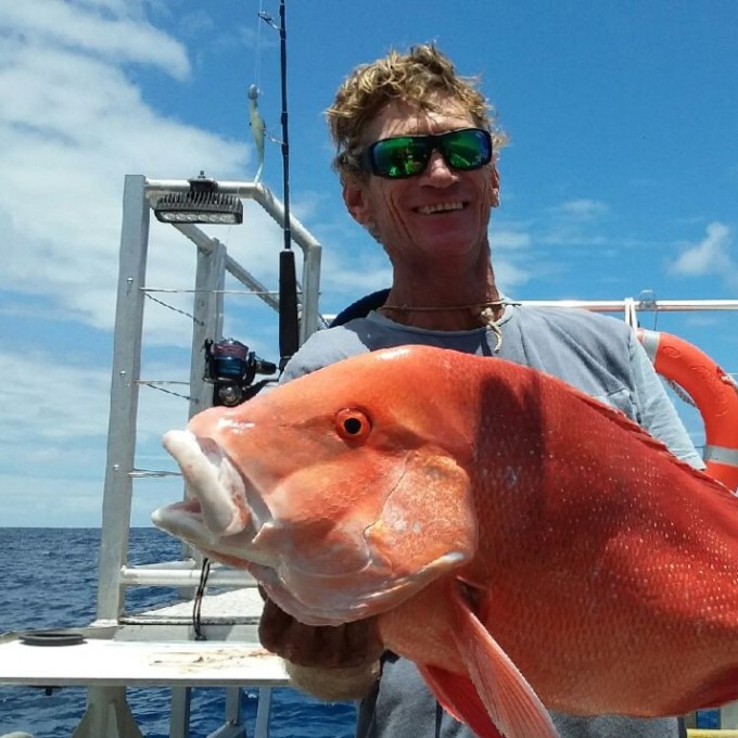 a man posing for the camera holding up the fish he caught with airlie beach fishing charters in airlie beach, queensland