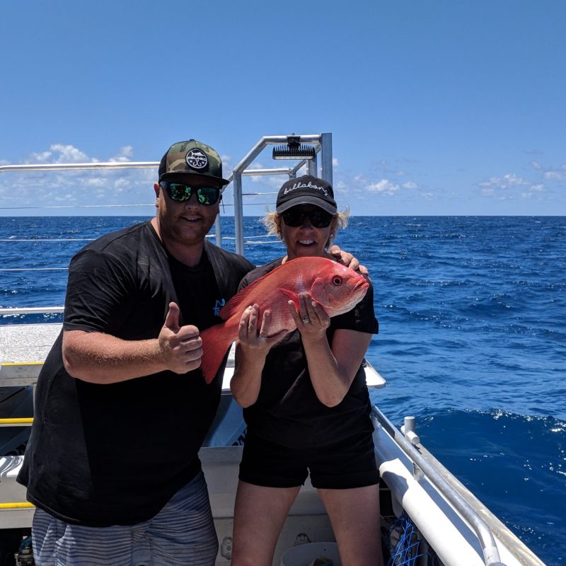 couple posing for the camera holding up the fish they caught with airlie beach fishing charters in airlie beach, queensland