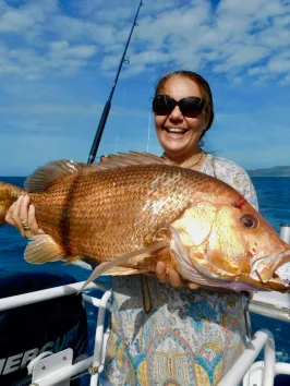 a woman posing for the camera holding up the fish she caught with airlie beach fishing charters in airlie beach, queensland