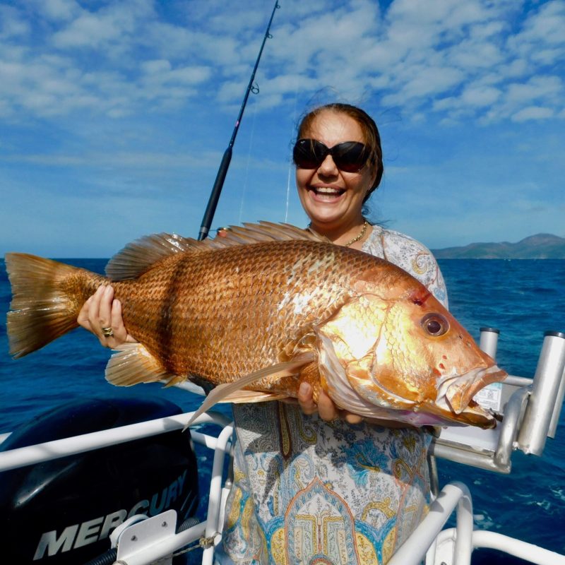 a woman posing for the camera holding up the fish she caught with airlie beach fishing charters in airlie beach, queensland