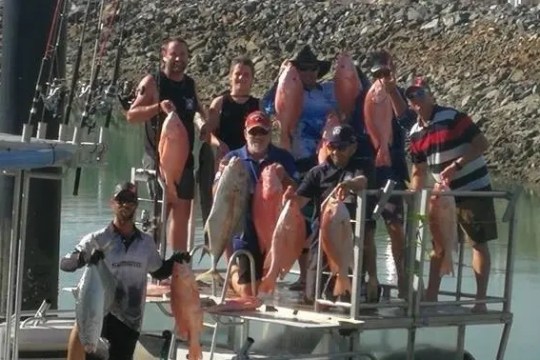 Group of people holding large fish on a dock by water.